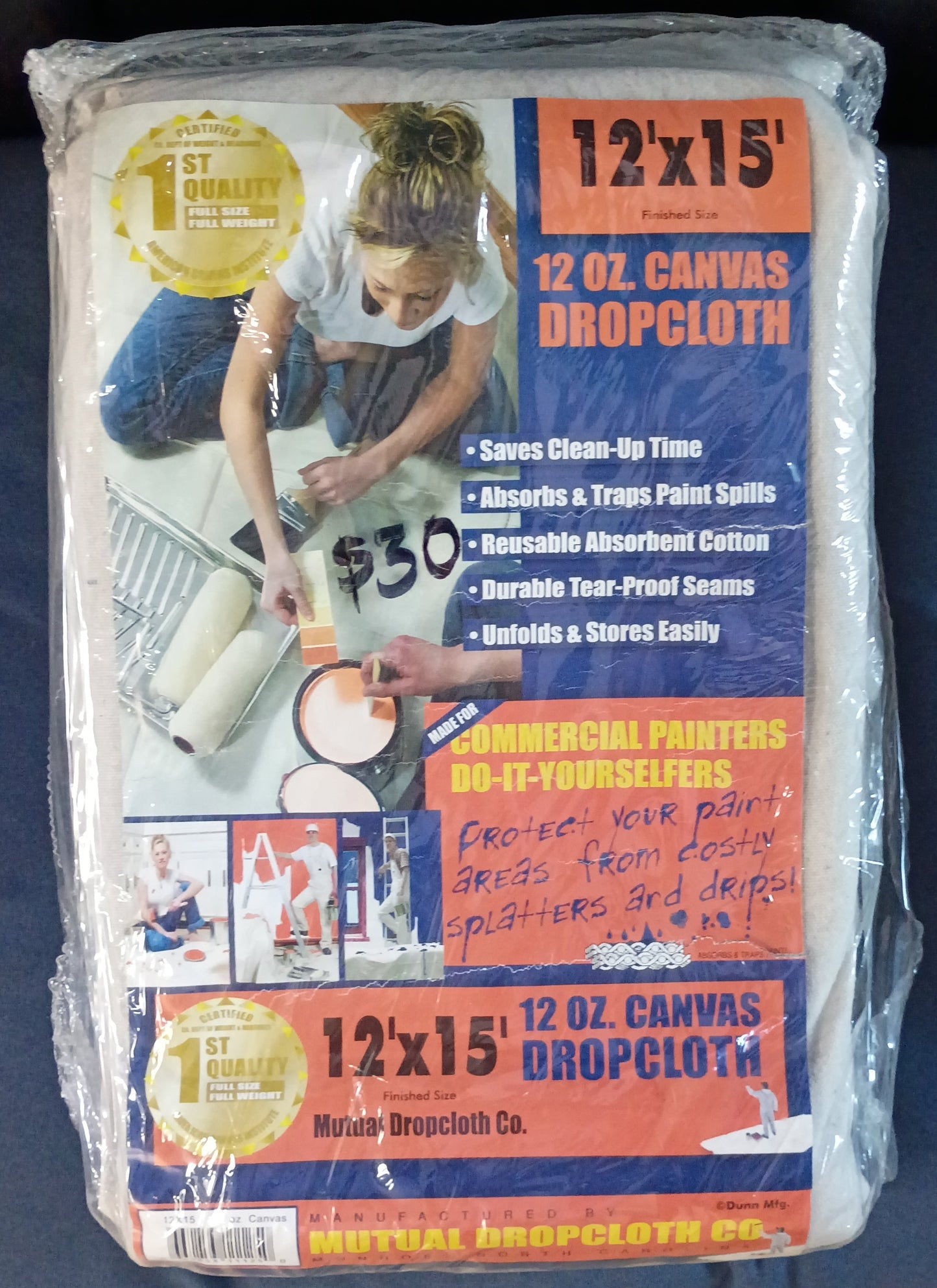 A package of Mutual Dropcloth Co. 12 oz canvas dropcloth in the 12x15' size, wrapped in clear plastic and displayed on a dark blue fabric surface.