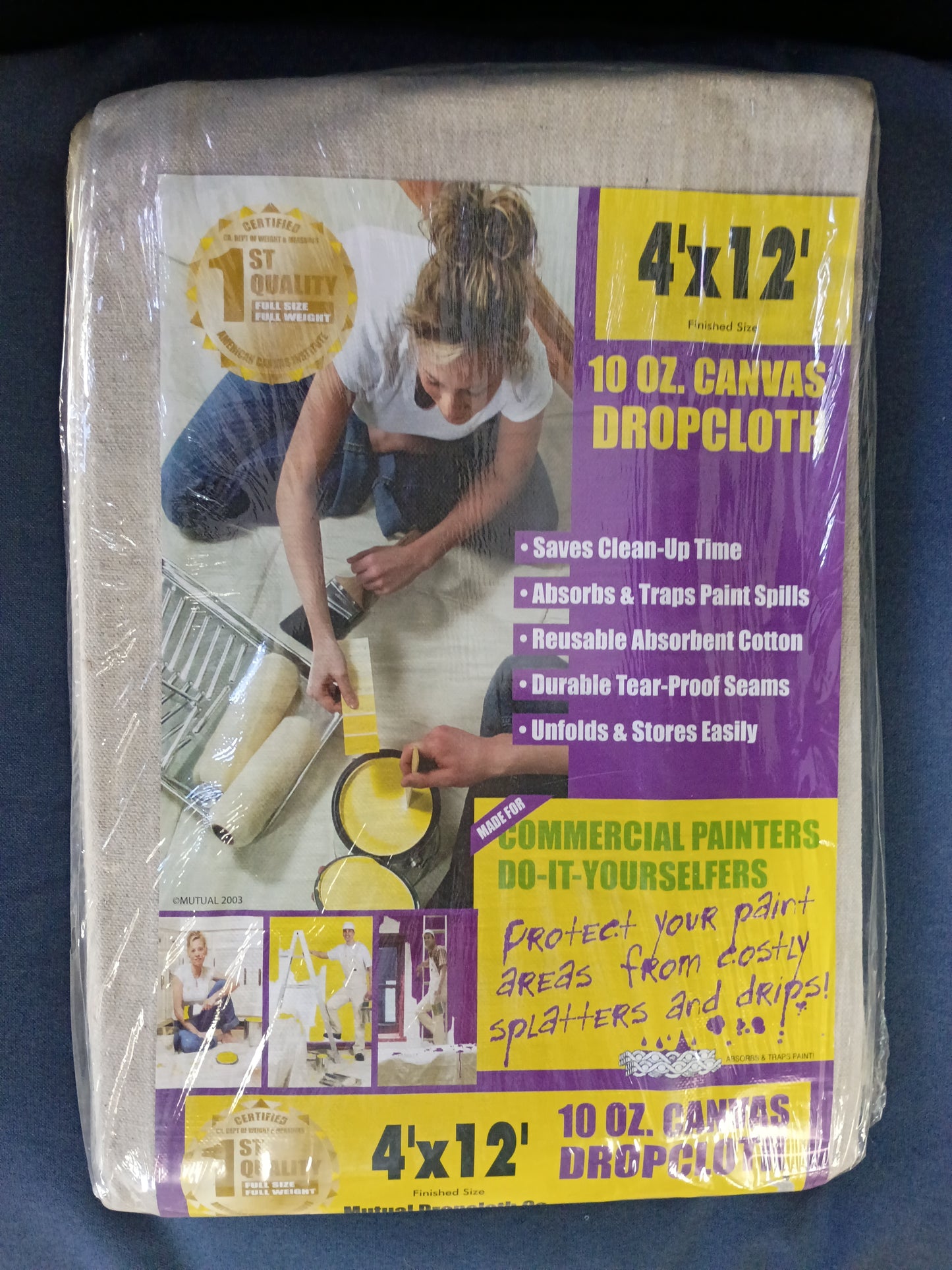 A packaged 4'x12' 10 oz canvas dropcloth by Mutual Dropcloth Co., sealed in clear plastic wrap. The packaging features a large photo of a woman painting, with prominent yellow and purple text blocks detailing the product features.