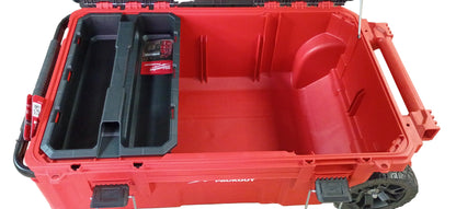 A red and black rugged Milwaukee rolling tool box with an open lid, shown on a white background. The case has molded interior compartments, including a black organizer tray on the left with a visible Milwaukee logo sticker.