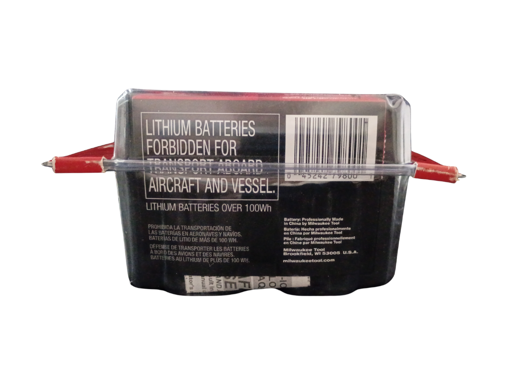 A sealed rectangular milwaukee brand lithium battery pack laying on it's back, photographed against a plain white background. The front has a large warning label reading 'LITHIUM BATTERIES FORBIDDEN FOR TRANSPORT ABOARD AIRCRAFT AND VESSEL' and a barcode.